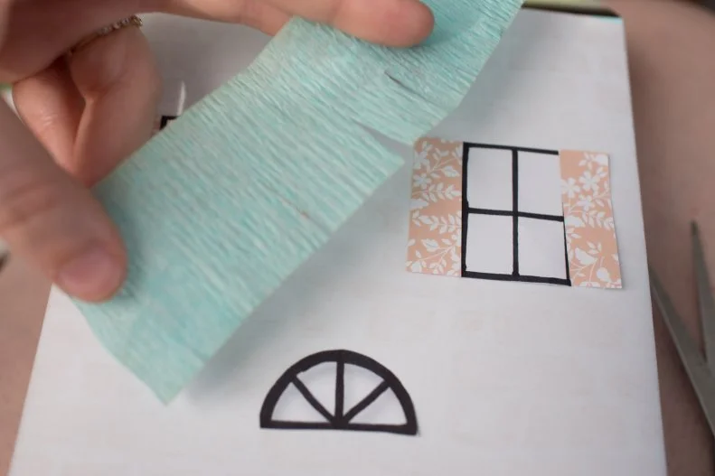 When it comes to making the roofs, you can use what you have on hand. If you have boxes that already have a roof shape from the folds of the box being taped together you can glue or tape pieces of streamers that have been cut to give the appearance of textured shingles. If you just want to use paper, cut a rectangle or triangle that’s the roughly the size of the container. Fold the rectangle in half and glue the inside of the triangle to the top of your box. If it’s a round container, roll your triangle and glue or tape the seam, then glue it to the top of the container. 