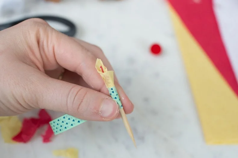 Use a small piece of yellow and red tissue paper and glue to the top of a toothpick or wooden skewer. Wind washi tape around the bottom of the tissue paper and then around the rest of the stick to create your candle. 