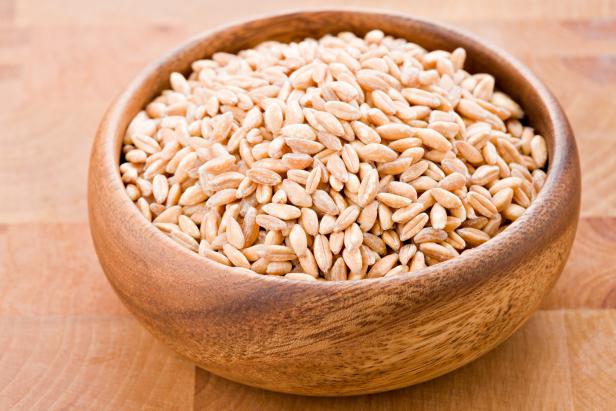 A high angle close up of farro in a round wooden bowl.Farro is related to wheat and is interchangeable with barley. Shot against a wooden butcher block cutting board.