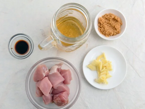 Chopped pork meat in a glass bowl and four marinade ingredients which are soy sauce, beer, brown sugar and chopped ginger. Decorative surface. High point of view.