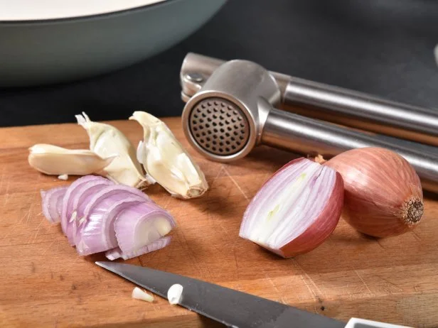 A sliced shallot with cloves of garlic on a cutting board