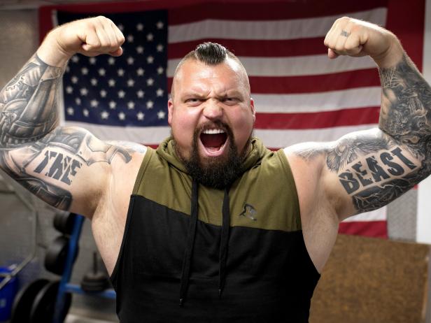 Eddie Hall flexing his muscles in front of the USA flag, as seen on Eddie Eats America, season 1.