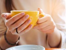Yellow mug in the hands of a young woman. Girl holding a Cup of coffee in a cafe. Coffee break, Breakfast. The concept of power. Close up.