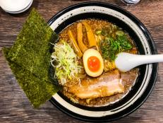 Tonkotsu and katsuobuhi kotteri soup ramen noodles with pork, fermented bamboo shoots, boiled egg and white and green spring onion toppings served in bowl on table