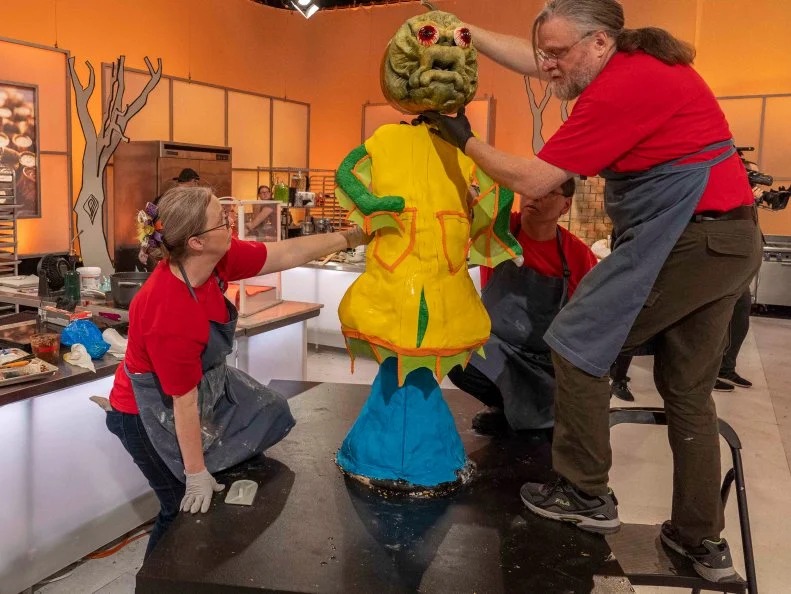 Left to Right: Team Ghoul-Icious Cake Maker Heather Sherman and Pumpkin Carver Deane Arnold install a carved pumpkin head atop their display during Episode 2 Spine Chiller challenge "Blind Date from Hell", as seen on Halloween Wars, Season 10.