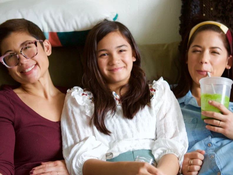 Candid moment of Molly Yeh and her sisters together on a couch in between takes while filming