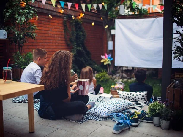 Group of children on movie night in backyard. Sitting on pillows, eating popcorn and watching movie.