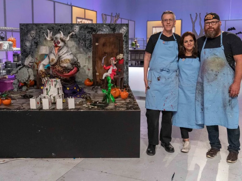 Halloween Wars, Season 10 winner team Mummies Rejects, Left to Right: Sugar Expert Steve Weiss, Cake Maker Helmata Basumatary, and Pumpkin Carver Daniel Miller pose next to their winning creation, as seen on Halloween Wars, Season 10.
