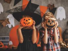 Boy and a girl are playing at the Halloween party, covering their faces with Jack O'Lantern bucket and paper bag.
