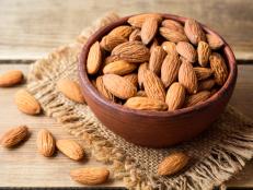 Almonds in ceramic bowl on wooden background. Selective focus.