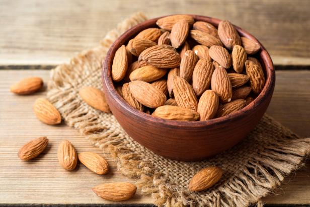 Almonds in ceramic bowl on wooden background. Selective focus.