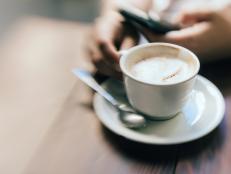 Closeup shot of a woman having a cup of coffee at a cafe while using mobile phone.