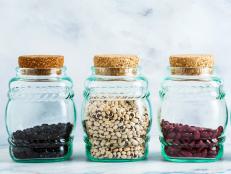 different types of legumes in glass jars with cork lids on a marble background