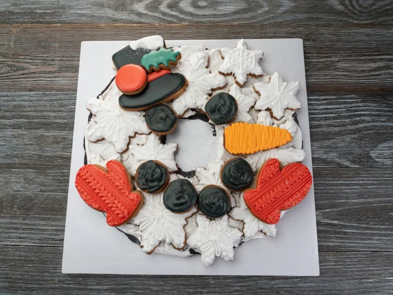 Contestant Jacqueline's Snowman wreath design comprised of Wreath Base: Double dark chocolate truffle with butter vanilla icing.Second dough:  Brown butter snickerdoodle with butter vanilla icing, as seen on Christmas Cookie Challenge, Season 4.