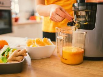 Mid adult woman making cold-pressed juice in the kitchen. Focus on cold-pressed juicer