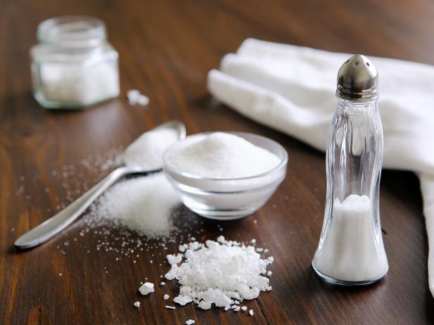 Natural, organic, sea, white salt in a spoon, in a Cup, in a salt shaker, poured on a wooden table. Next to the linen towel. The concept of cooking healthy food, cosmetology. Selective focus