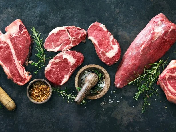 Variety of raw beef meat steaks for grilling with seasoning and utensils on dark rustic board