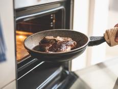 Close up of male hand holding frying pan with delicious beef steak near electric oven