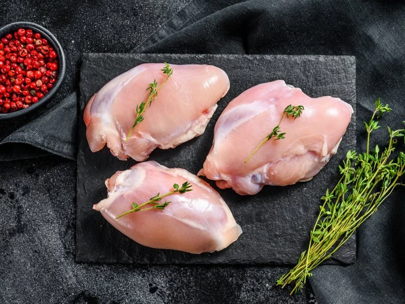 Raw boneless chicken thighs fillet. Black background. Top view.