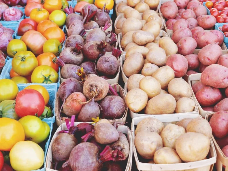 Variety of fresh fruits and vegetables on a table at a farmers market.