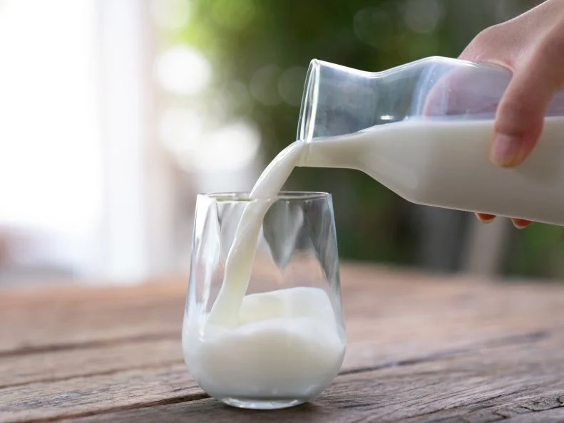 The milk is poured into a ceramic jug into a glass on a natural background.