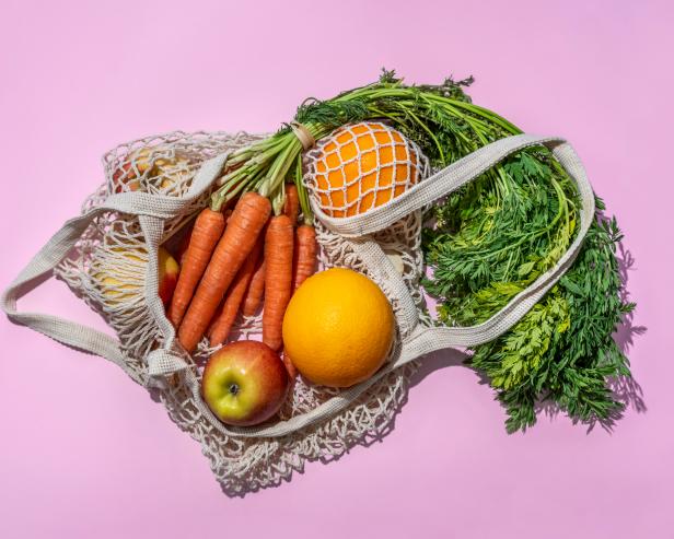 Reusable cotton mesh bag with fruit and vegetables on pink background. Zero Waste shopping concept.