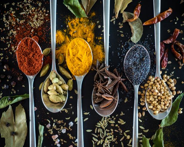 Variety of spices on spoon against black background. Paprika, poppy seeds, star anis, cardamom, curry, turmeric, fenchel seeds, bay leaves, curry leaves, coriander seeds, dried chillies, black pepper