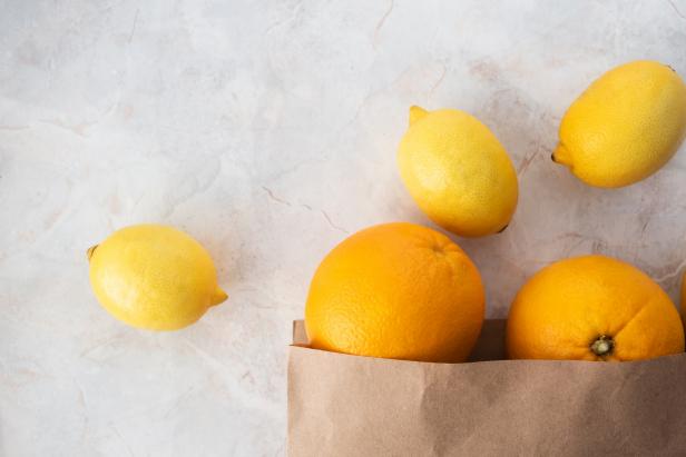 Close-up lemons and oranges in paper shopping bag on marble table, top view. Zero waste eco friendly. Horizontal format