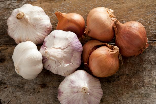 Fresh raw whole garlic bulbs and brown onions, both of the Allium family, on a rustic wooden table viewed from overhead