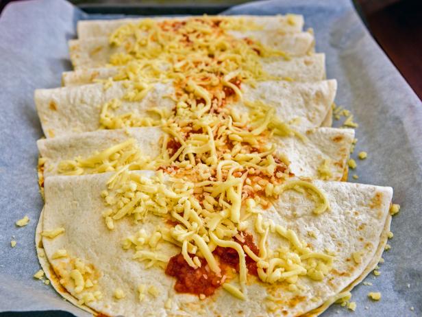 Homemade traditional Mexican food burrito, fajitas, Quesadillas, Enchiladas or tacos with cheddar cheese on a backing paper, ready for baking in the oven.