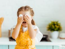 funny kid in yellow polka dot apron holding eggs in front of eyes in kitchen