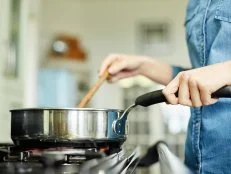 Midsection below view image of woman cooking food in pan. Utensil is placed on gas stove. Female is stirring dish in frying pan. She is preparing food in domestic kitchen.