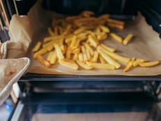 A woman takes the french fries from the oven.