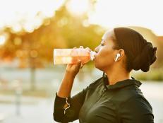 Muslim woman drinking sports drink after working out in park on fall afternoon