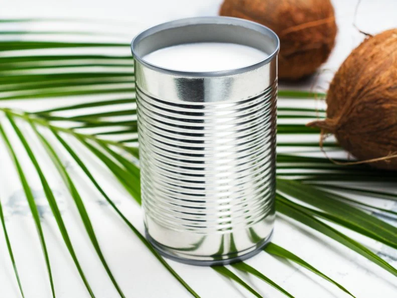 Opened tin can with coconut milk drink. Alternative non dairy vegan milk on white stone table