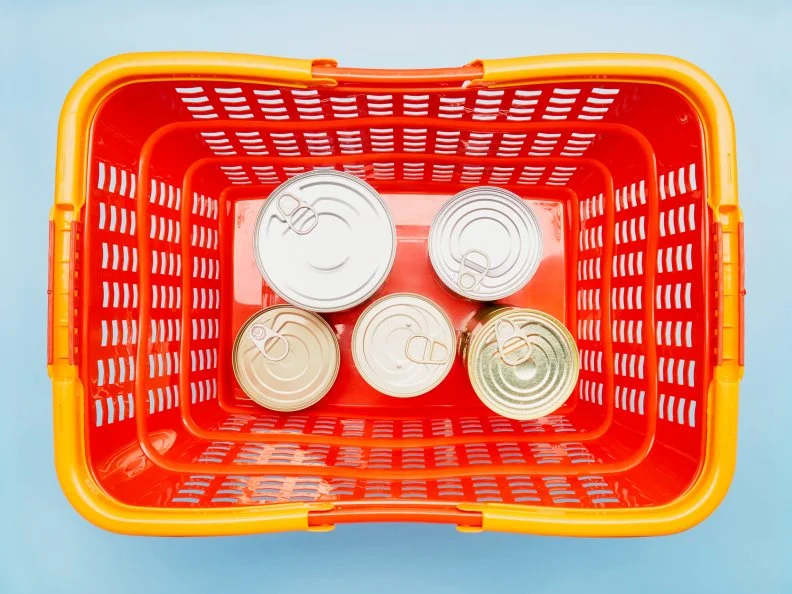 Still life of canned food in red shopping basket on blue background