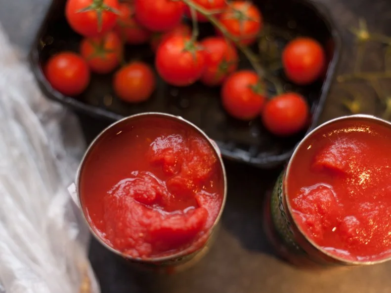 Fresh cherry tomatoes (on the vine) and two open cans of tomatoes on a kitchen counter