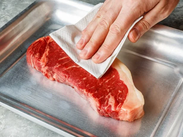 Raw fresh meat Steak Striploin in aluminum tray drying up excess moisture by Male hand with paper towel