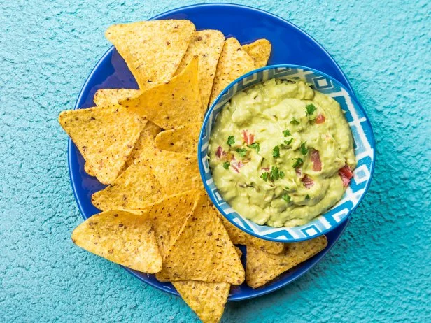 Mexican nachos, tortilla chips with guacamole sauce over blue background, top view