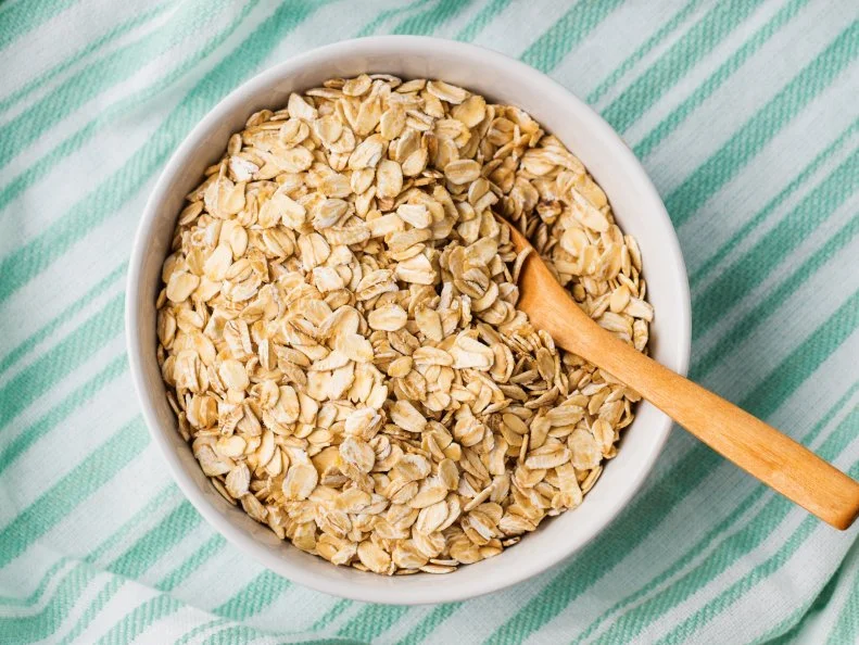 Gluten free oatmeal flakes in white bowl on green turquoise napkin background. Overhead closeup