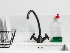 A sink and tap and washing up liquid in a white clean and organised sink and kitchen. The plates and drainer are organised and clean and the tap has water coming from it