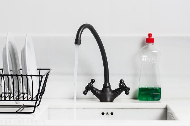 A sink and tap and washing up liquid in a white clean and organised sink and kitchen. The plates and drainer are organised and clean and the tap has water coming from it