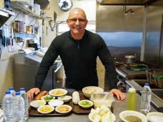 Chef Robert Irvine showing off ingredients in the kitchen at The Anchor, as seen on Restaurant: Impossible, season 18.