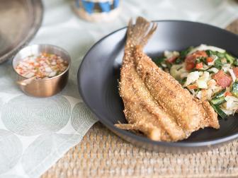 Fried fish with collard greens plated on woven table, as seen on The Juneteenth Menu