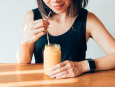 Close-up shot of smiling young woman drinking fresh mango smoothie at cafe.