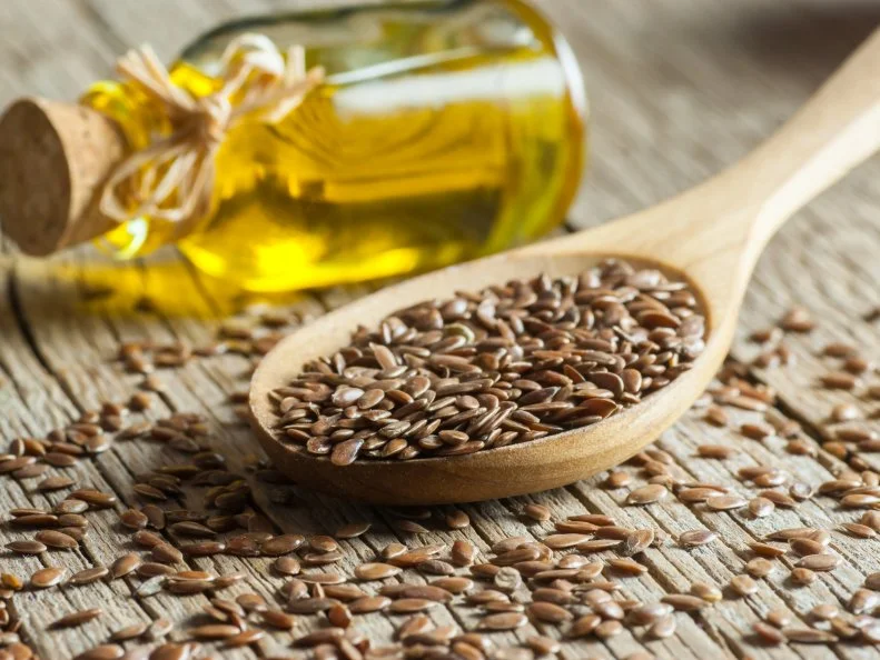 Heap of Flax seeds or linseeds in spoon with glass of linseed oil on wooden backdrop. Flaxseed or linseed concept. Flax seed dietary fiber