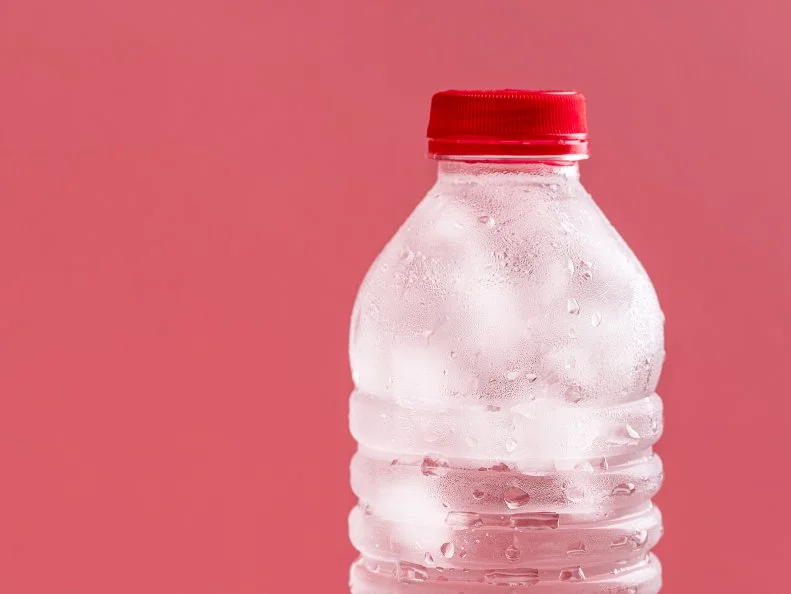 Plastic bottle with water and ice cubes close-up on a pink background. Cold natural water in a bottle. Fresh cold   drink