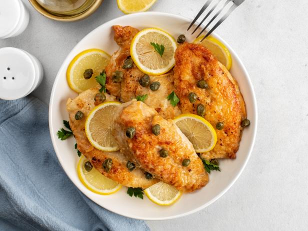 Chicken piccata on white table directly above. Chicken breast dredged in flour and cooked in sauce cantaining lemon juice, butter and capers.