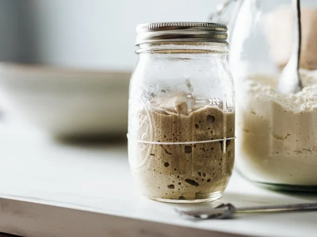 Close-up of sourdough starter and flour in jars. Yeast is on kitchen counter. It is in glass container.