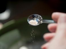 Woman adding yeast to a bowl with flour for bread making. Close up of yeast grains falling, lit by the sun and seen from a personal perspective.